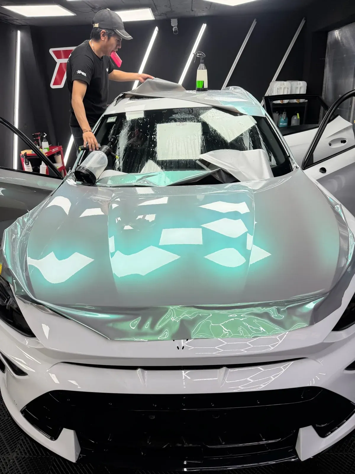 Instalador colocando película de color verde menta sobre el cofre blanco de un Cupra